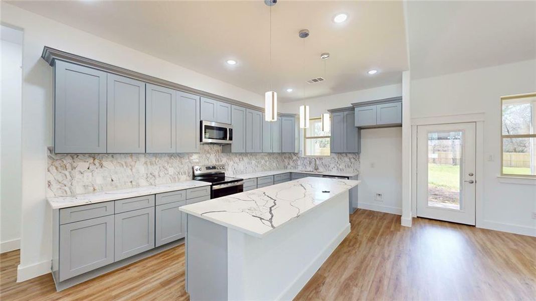 Kitchen featuring stainless steel appliances, tasteful backsplash, gray cabinets, light stone countertops, and light wood-type flooring