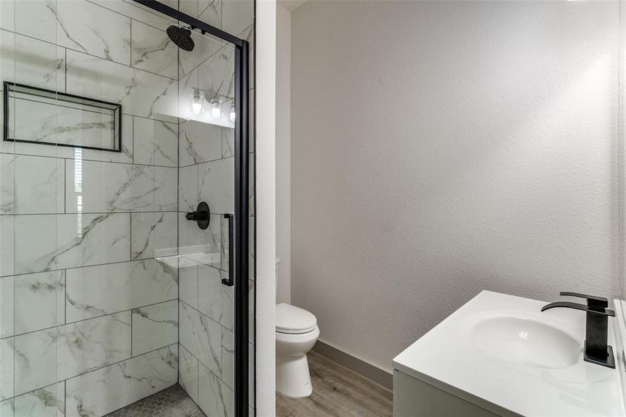 Bathroom with vanity, a marble finish shower, light wood finished floors, and a textured wall Bathroom with vanity, a marble finish shower, light wood finished floors, and a textured wall