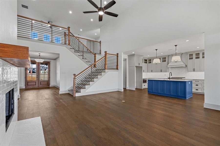 Unfurnished living room with a high ceiling, ceiling fan with notable chandelier, dark hardwood / wood-style floors, and sink