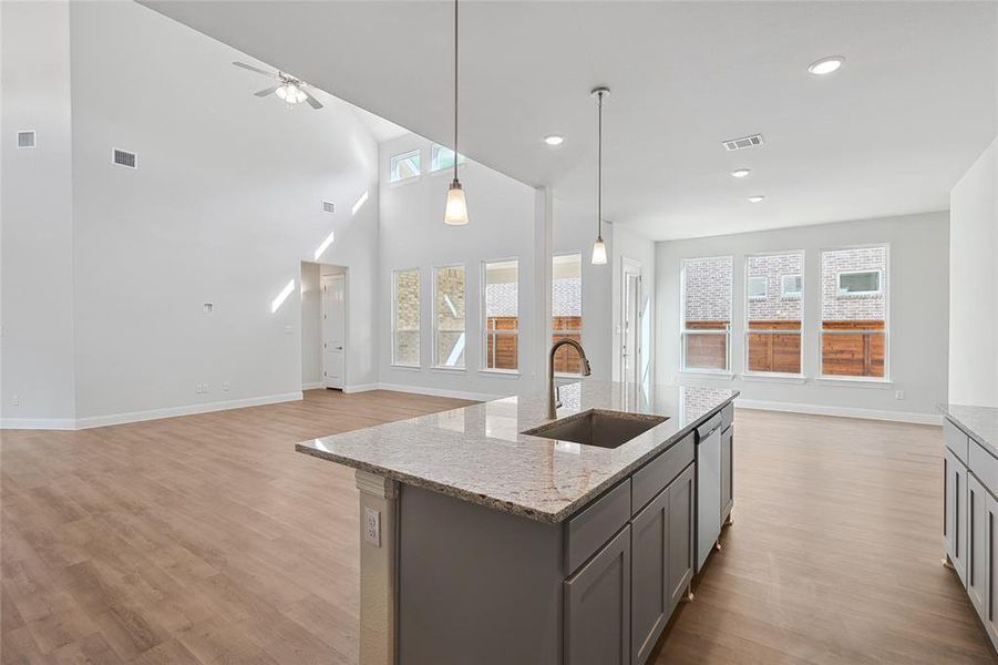 Kitchen with open floor plan, a high ceiling, gray cabinets, an island with sink, and light stone countertops Kitchen with open floor plan, a high ceiling, gray cabinets, an island with sink, and light stone countertops