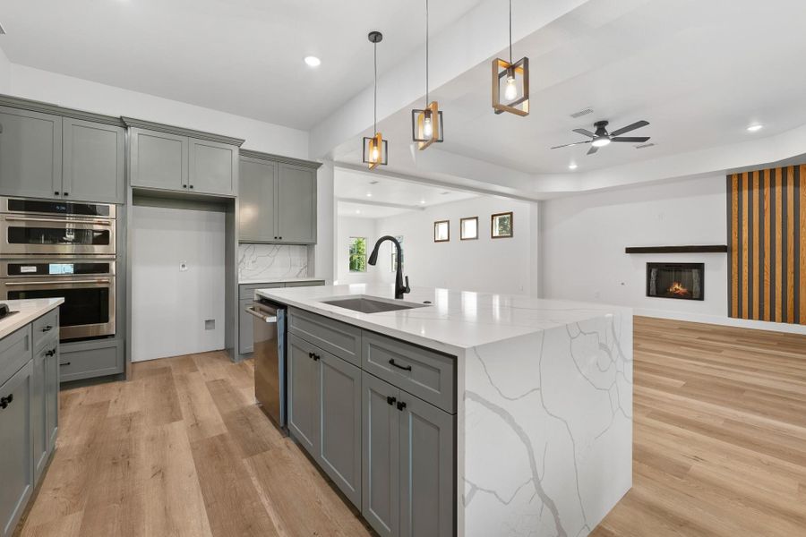 This kitchen features modern design elements with sleek gray cabinets, a large marble island with a waterfall edge, and stylish pendant lighting. It has stainless steel appliances, a built-in range hood, and hardwood floors, creating a contemporary and inviting space. This kitchen features modern design elements with sleek gray cabinets, a large marble island with a waterfall edge, and stylish pendant lighting. It has stainless steel appliances, a built-in range hood, and hardwood floors, creating a contemporary and inviting space.