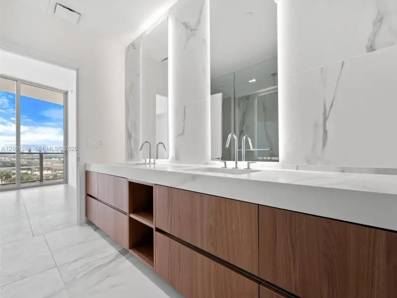 Floating wood-finish vanity with stone countertop, dual integrated sinks, floor-to-ceiling stone wall cladding, and illuminated mirrors Floating wood-finish vanity with stone countertop, dual integrated sinks, floor-to-ceiling stone wall cladding, and illuminated mirrors