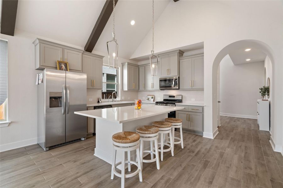 The bright kitchen boasts a large center island/breakfast bar, quartz countertops, and gorgeous light fixtures.