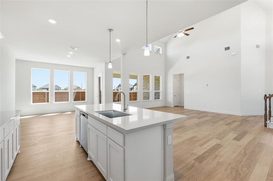 Kitchen featuring open floor plan, light wood finished floors, plenty of natural light, an island with sink, and a high ceiling