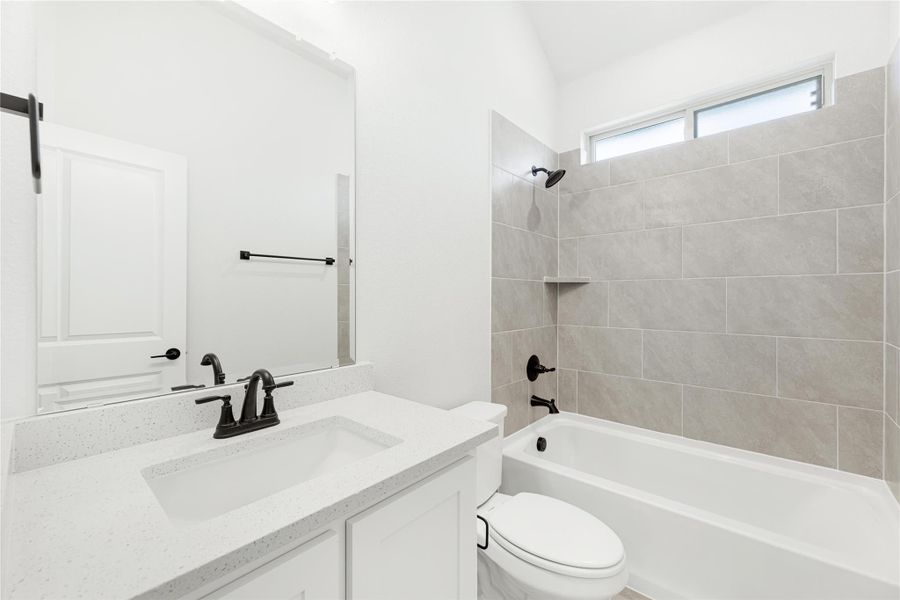 Bathroom with white vanity, quartz countertop, and tiled shower-tub combo with black fixtures