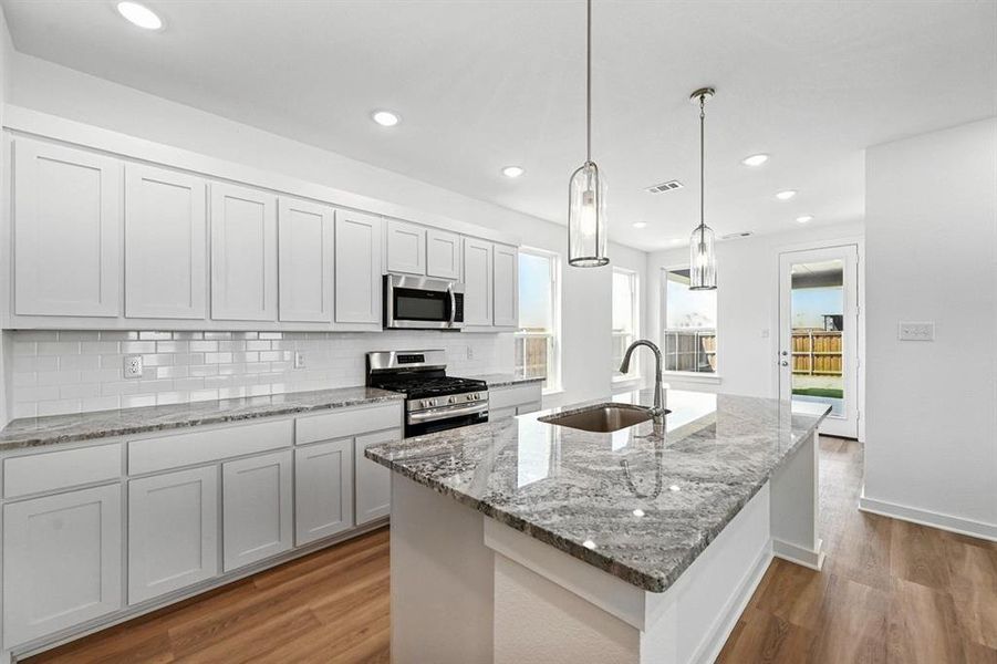 Kitchen featuring stainless steel appliances, white cabinets, a kitchen island with sink, light stone countertops, and dark wood finished floors