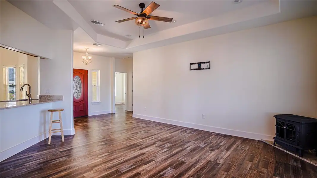 Ready to move in living room featuring a tray ceiling, ceiling fan, a wood stove, suspended lighting, and wood finished floors Ready to move in living room featuring a tray ceiling, ceiling fan, a wood stove, suspended lighting, and wood finished floors