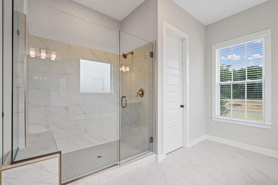 Spacious walk-in shower featuring clear glass enclosure, white rectangular wall tiles with subtle veining, a built-in shower bench with bronze trim, and a bronze shower fixture Spacious walk-in shower featuring clear glass enclosure, white rectangular wall tiles with subtle veining, a built-in shower bench with bronze trim, and a bronze shower fixture