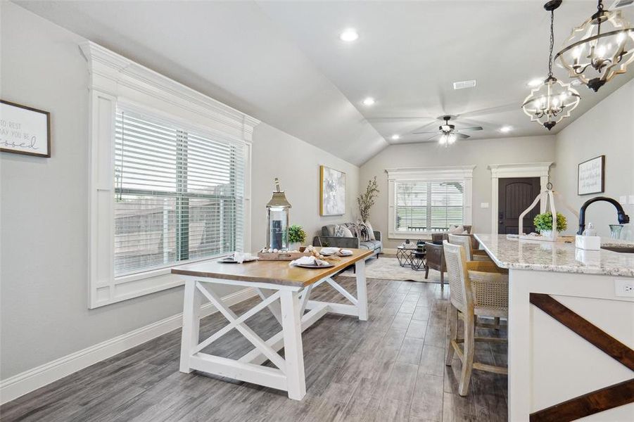 Kitchen with ceiling fan with notable chandelier, hardwood / wood-style floors, lofted ceiling, hanging light fixtures, and light stone countertops