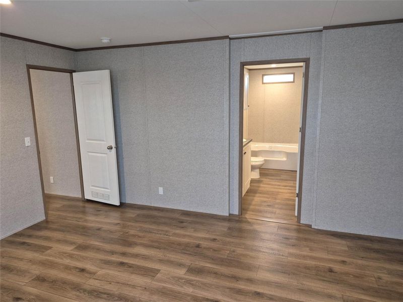 Unfurnished bedroom featuring ensuite bathroom, dark wood-type flooring, and crown molding