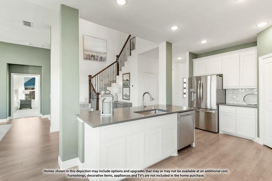 Kitchen with white island, gray countertops, stainless steel appliances, and staircase visible in background Kitchen with white island, gray countertops, stainless steel appliances, and staircase visible in background