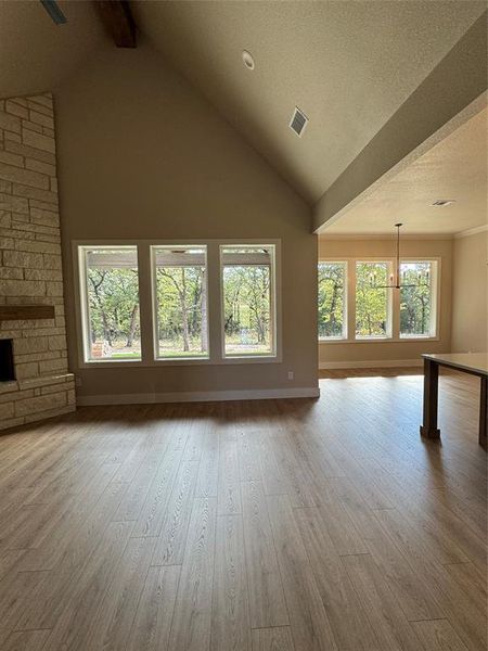 Unfurnished living room with beam ceiling, light wood-type flooring, high vaulted ceiling, a textured ceiling, and a stone fireplace Unfurnished living room with beam ceiling, light wood-type flooring, high vaulted ceiling, a textured ceiling, and a stone fireplace