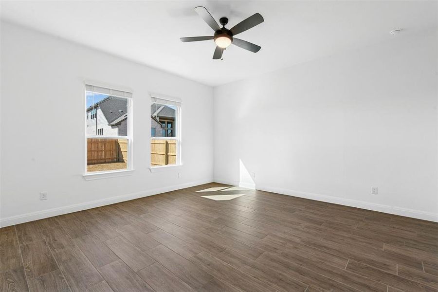 Spacious room featuring wood-finish flooring, white walls, two large windows, and a ceiling fan with integrated lighting