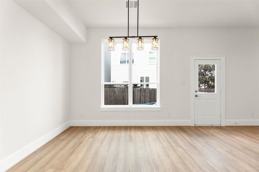 Bright, open room with modern pendant lighting, and large window offering natural light. Access to the outdoors through a door with a view of the fenced yard.