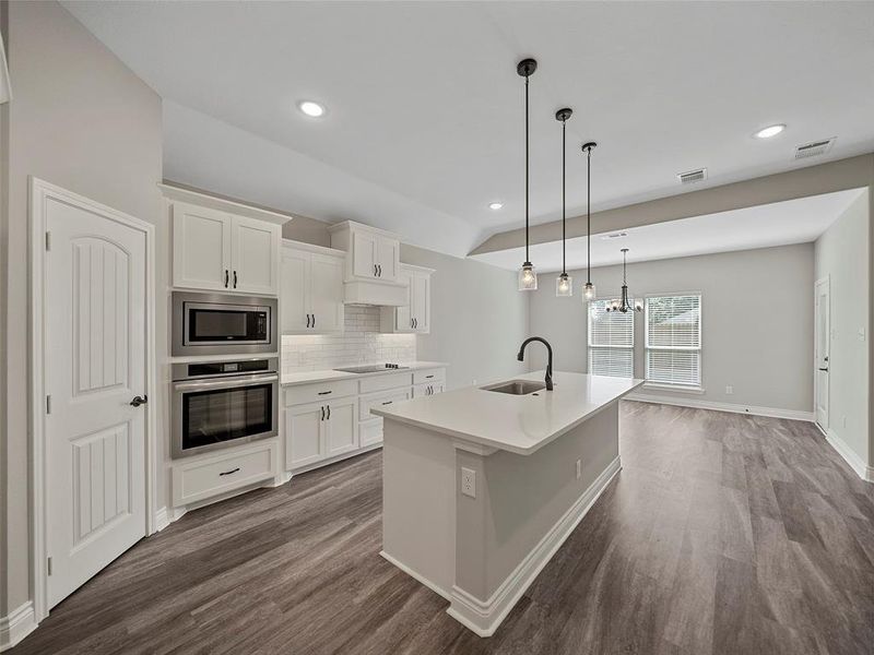 Kitchen featuring tasteful backsplash, appliances with stainless steel finishes, white cabinets, decorative light fixtures, and dark wood finished floors Kitchen featuring tasteful backsplash, appliances with stainless steel finishes, white cabinets, decorative light fixtures, and dark wood finished floors