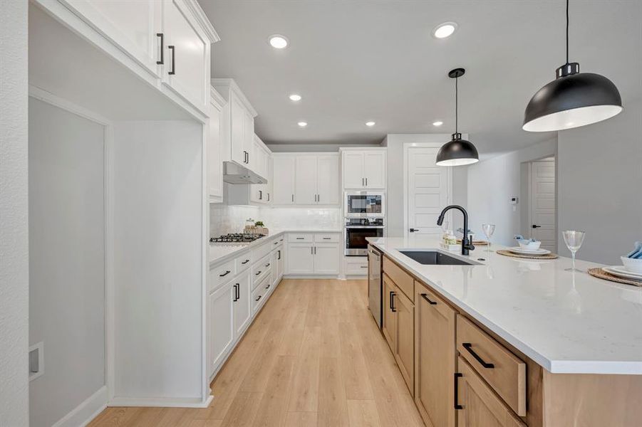 Kitchen with dual tone cabinets, light wood-type flooring, tasteful backsplash, decorative light fixtures, and light stone counters