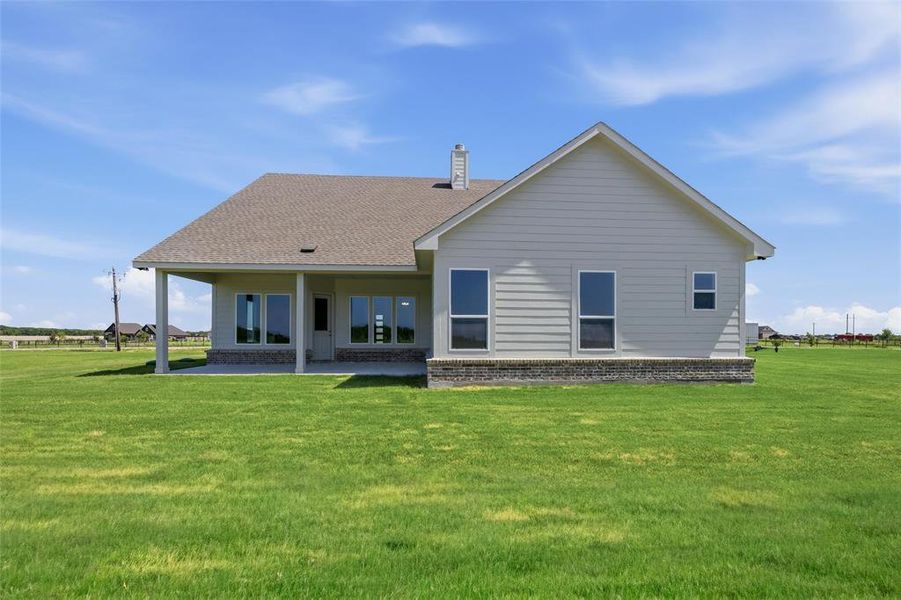 Rear exterior featuring a covered patio, multiple windows, light-colored siding, and a brick wainscoting foundation Rear exterior featuring a covered patio, multiple windows, light-colored siding, and a brick wainscoting foundation