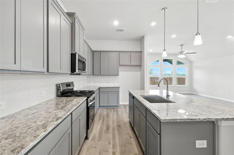 Kitchen featuring stainless steel appliances, gray cabinetry, a center island with sink, light wood-style flooring, and ceiling fan