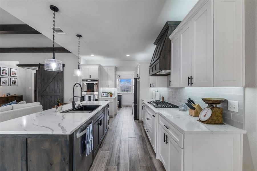 Kitchen with white cabinetry, light stone counters, decorative light fixtures, a large island with sink, and a barn door