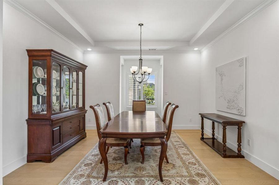 Dining area with hanging lights, light wood-style flooring, crown molding, and a tray ceiling
