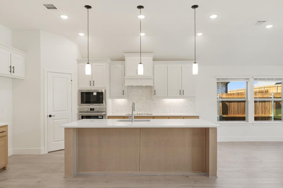 Kitchen with large wood island, white cabinets, pendant lights, and stainless steel appliances