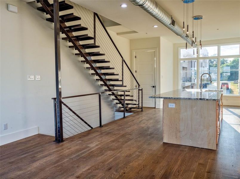 Kitchen with stone counters, dark hardwood / wood-style floors, a kitchen island with sink, and hanging light fixtures