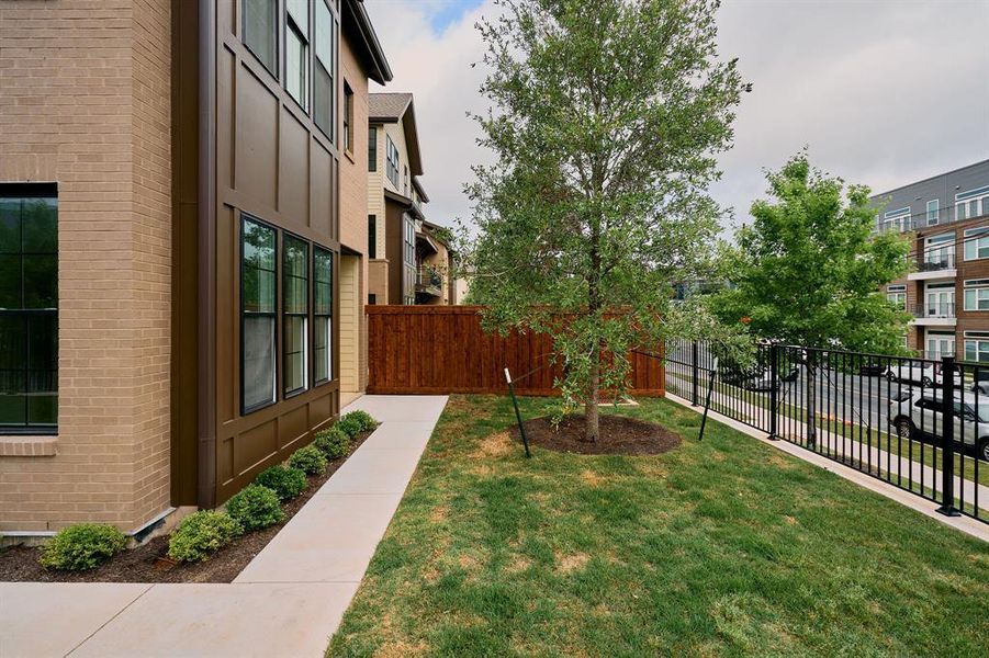 Exterior featuring a brick facade, contemporary brown siding, multiple large windows, a concrete walkway, and a manicured lawn with a young tree Exterior featuring a brick facade, contemporary brown siding, multiple large windows, a concrete walkway, and a manicured lawn with a young tree