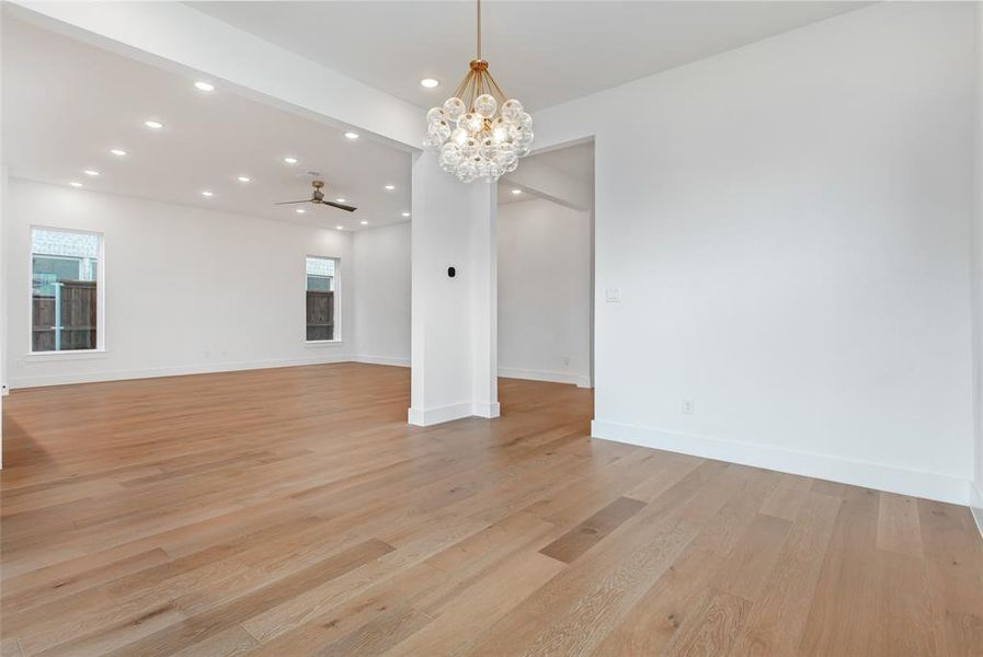 Unfurnished living room with beam ceiling, ceiling fan with notable chandelier, and light wood-type flooring