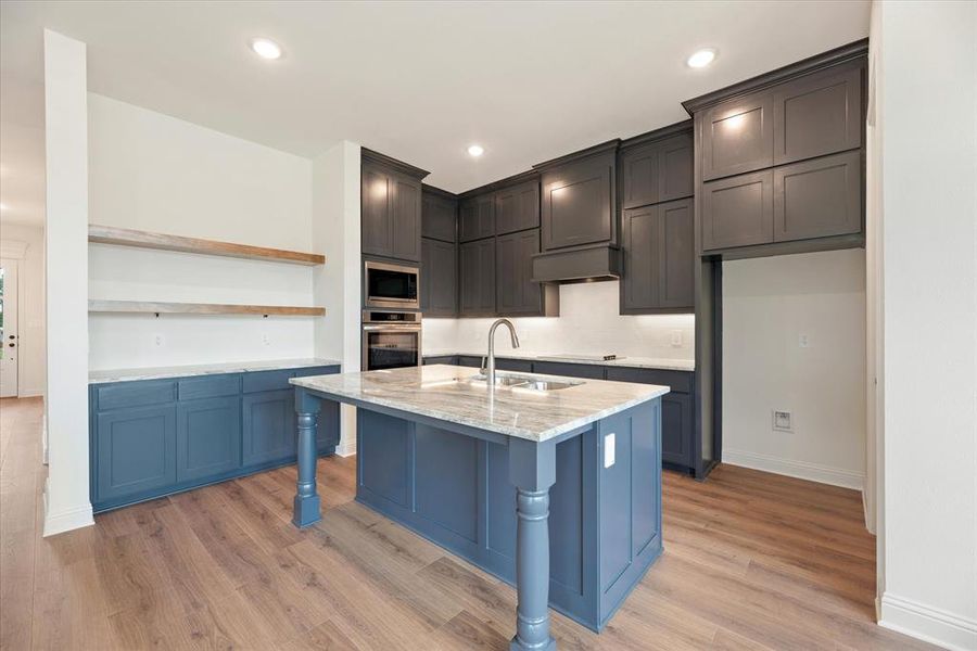 Kitchen featuring a kitchen island with sink, light hardwood / wood-style flooring, sink, light stone countertops, and appliances with stainless steel finishes