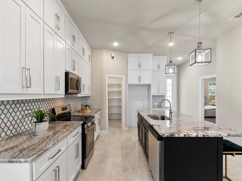 Kitchen featuring pendant lighting, sink, a center island with sink, white cabinetry, and appliances with stainless steel finishes