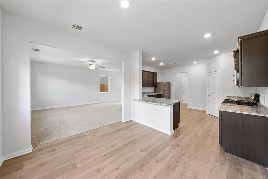 Kitchen with visible vents, dark brown cabinetry, open floor plan, a ceiling fan, and stainless steel appliances