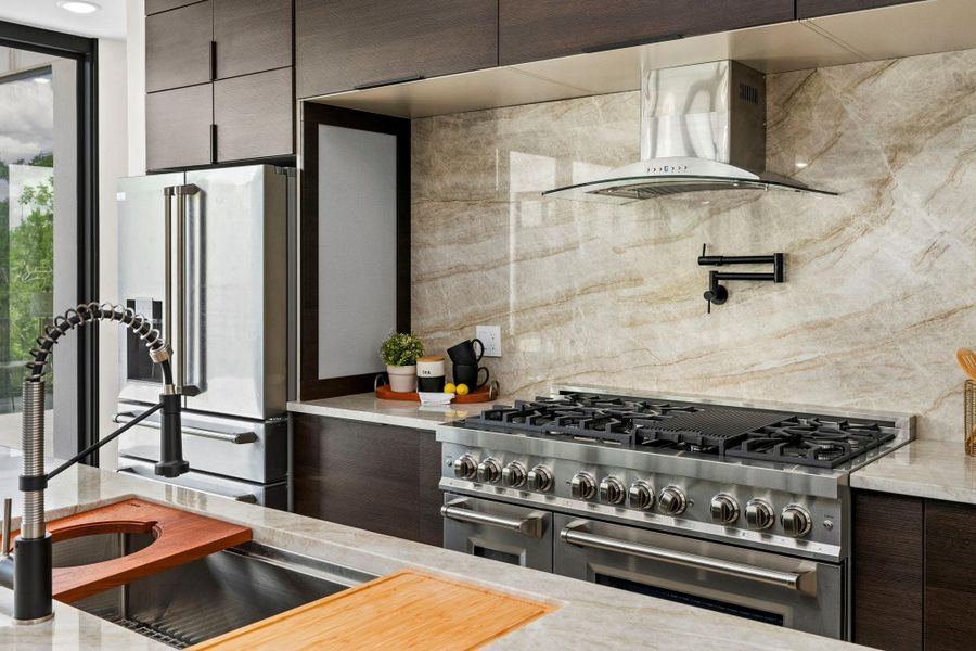 Kitchen featuring dark wood finish cabinetry, modern cabinets, high end appliances, light stone countertops, and decorative backsplash