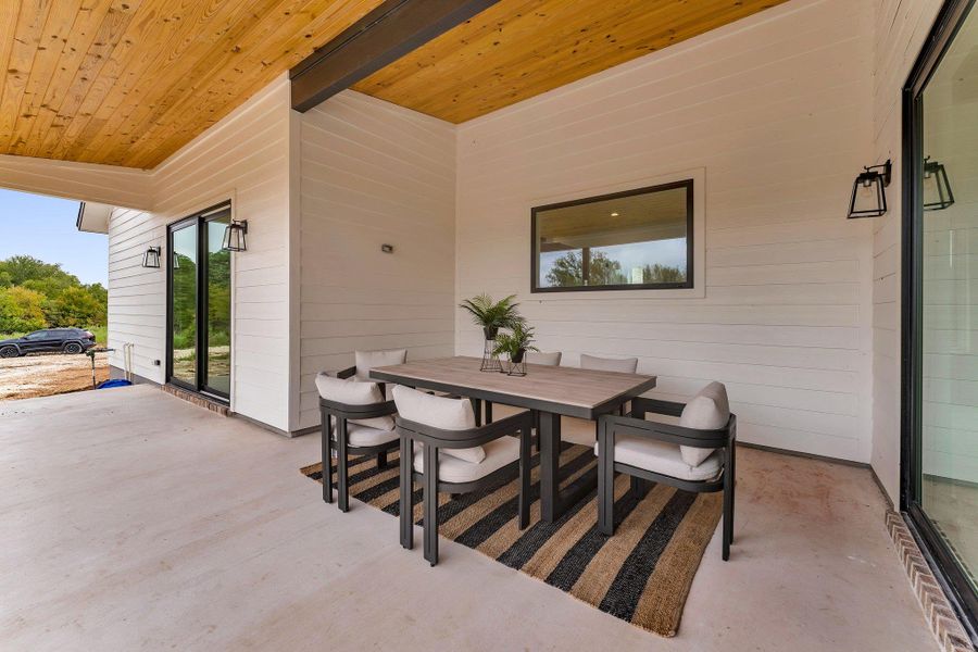 A welcoming covered patio with a wooden ceiling and concrete flooring, offering an ideal space for outdoor relaxation and dining. A welcoming covered patio with a wooden ceiling and concrete flooring, offering an ideal space for outdoor relaxation and dining.