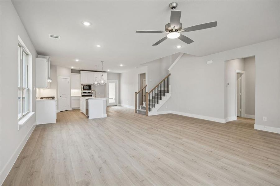 Unfurnished living room with recessed lighting, stairway, light wood-type flooring, a ceiling fan, and a chandelier Unfurnished living room with recessed lighting, stairway, light wood-type flooring, a ceiling fan, and a chandelier