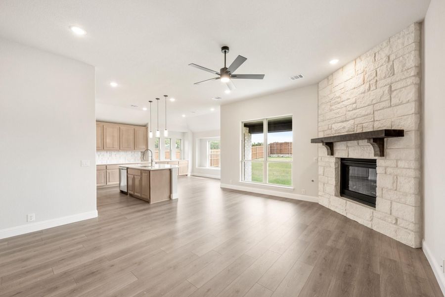 Open living area with stone fireplace, hardwood floors, and open-concept kitchen with island in background