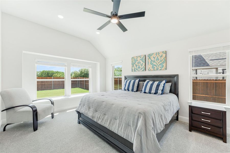 Bedroom with vaulted ceiling, ceiling fan, large windows, and dark wood furniture on carpet