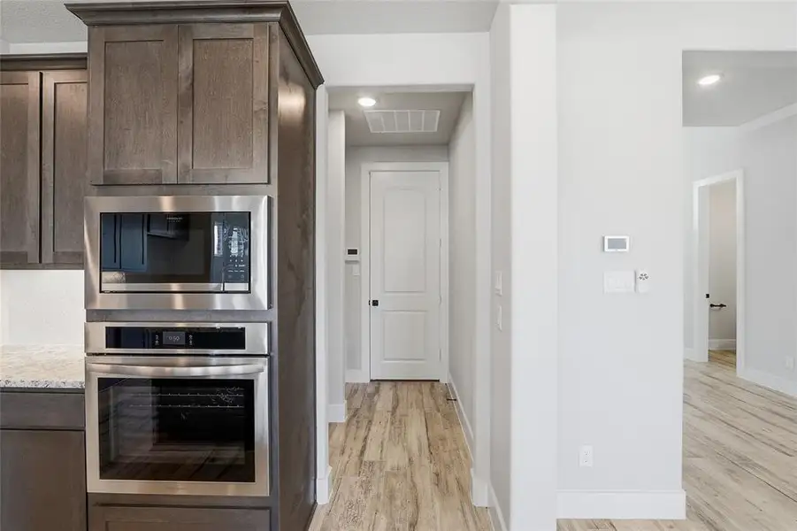 Kitchen with dark brown cabinetry, appliances with stainless steel finishes, light wood-style floors, light stone counters, and recessed lighting