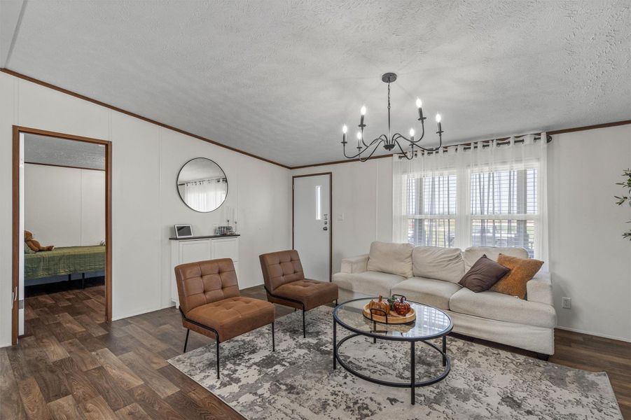 Living room with crown molding, dark wood-style floors, a textured ceiling, and a chandelier