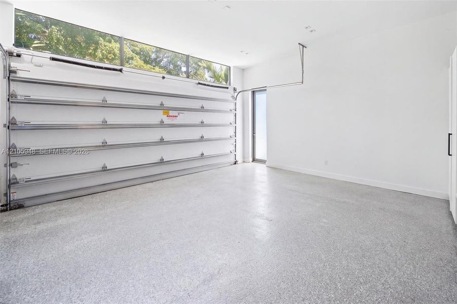 Garage space featuring speckled epoxy flooring, white paneled walls, a ceiling-mounted automatic door opener, and a row of horizontal transom windows