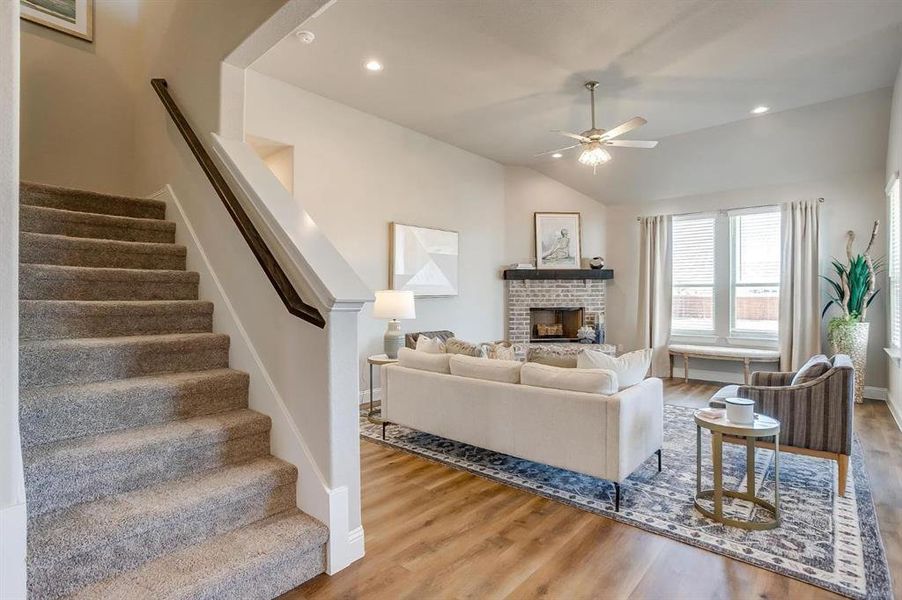 Living room featuring vaulted ceiling, wood-type flooring, a brick fireplace, and ceiling fan