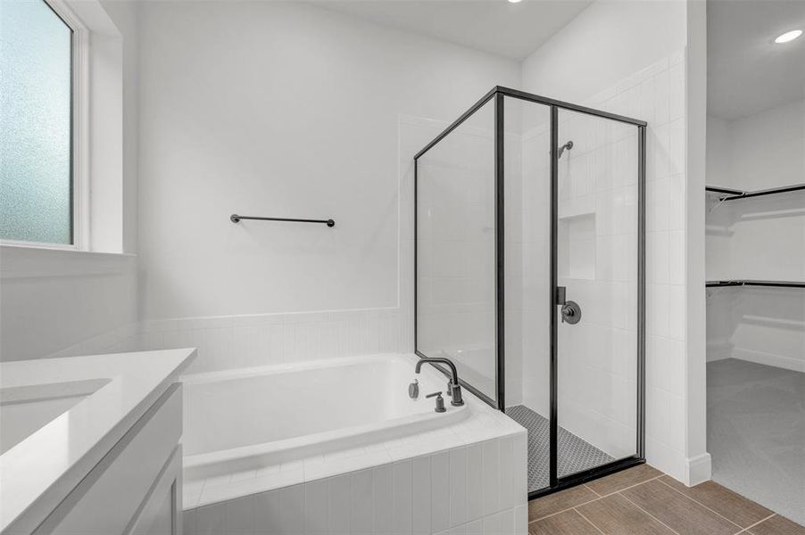 Bathroom featuring a white bathtub, a glass-enclosed shower with black framing, and a vanity with a white countertop