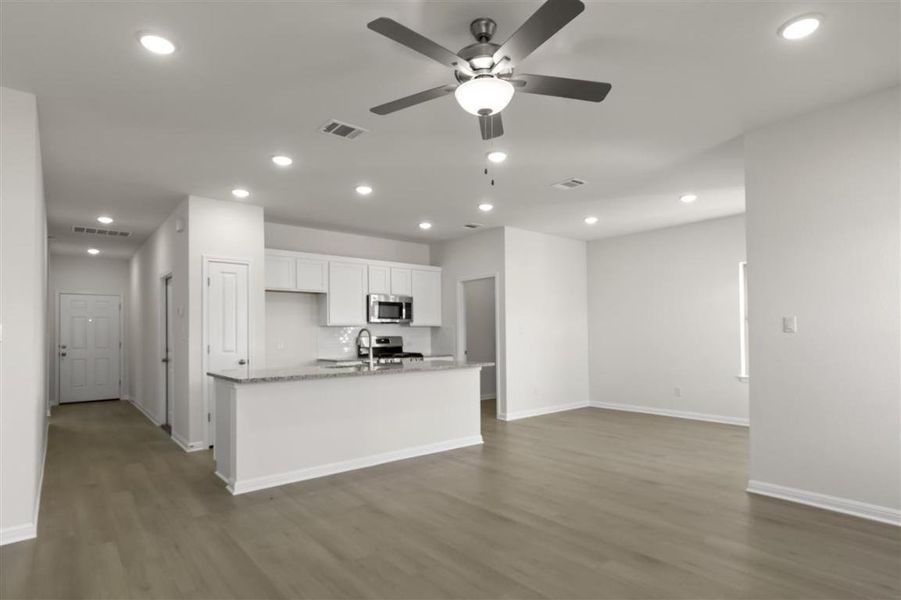 Kitchen featuring wood finished floors, a sink, white cabinetry, decorative backsplash, and stainless steel microwave