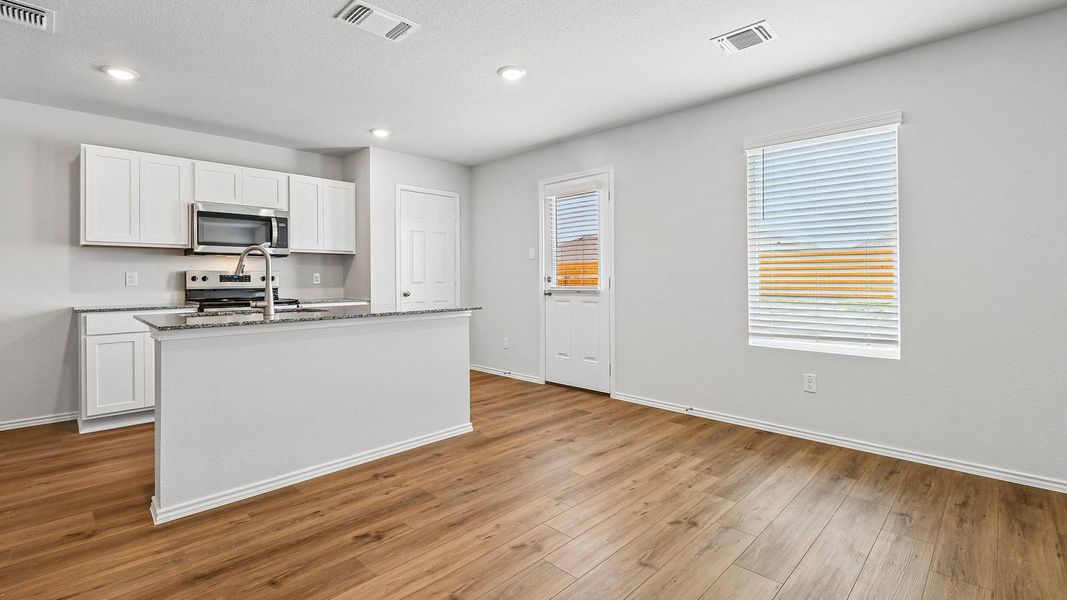 A well-lit kitchen and living area features rich wood flooring and a functional kitchen island with a breakfast bar.