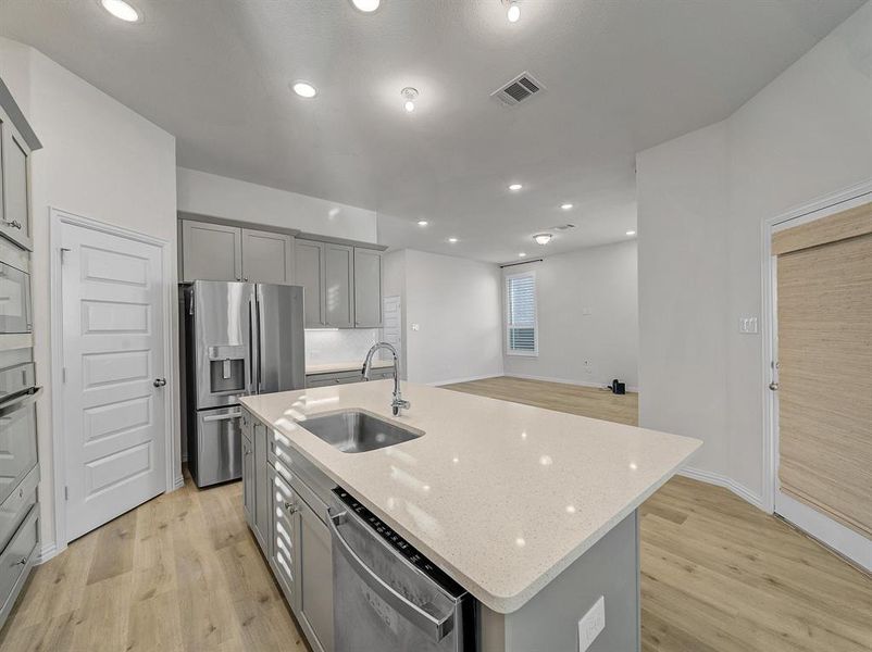 Kitchen with light stone countertops, sink, stainless steel appliances, an island with sink, and gray cabinets