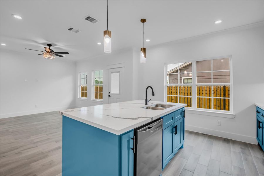 Discover a bright, open-concept kitchen and living room featuring sleek blue cabinetry, modern fixtures, and ample natural light, perfect for stylish living and entertaining.