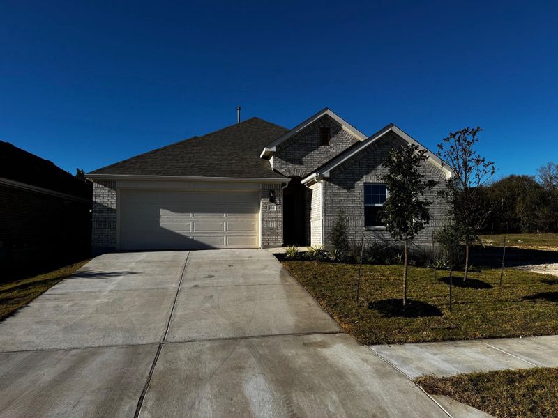 View of front facade featuring brick siding, a front lawn, driveway, and a garage
