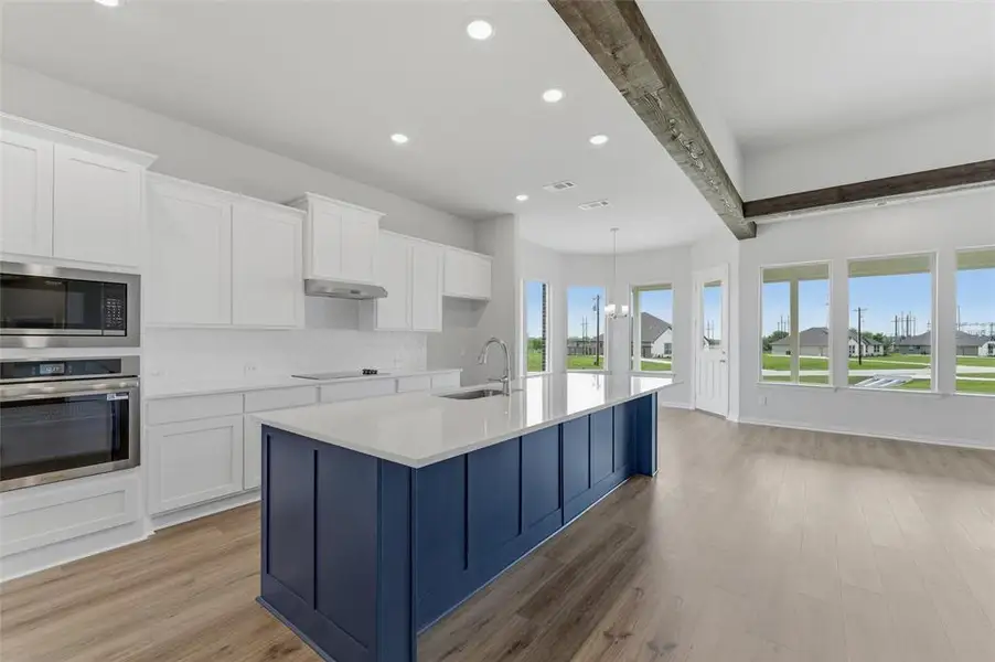 Open-concept kitchen and living area featuring a spacious island with a quartz countertop, stainless steel appliances, and large windows providing abundant natural light