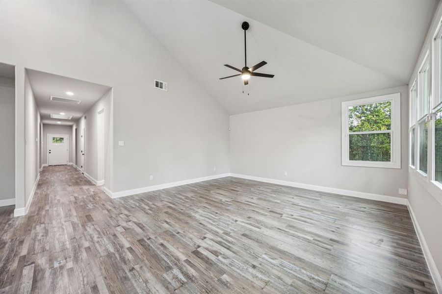 Family room on rear of home with high vaulted ceiling, light wood-style flooring, and ceiling fan. Point of view to the front of the home.