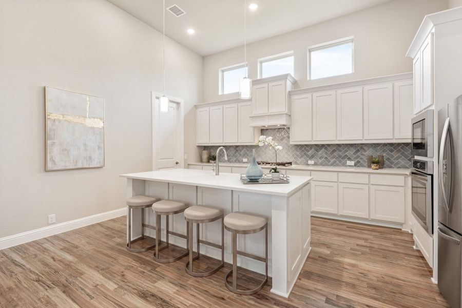 Kitchen with white cabinets, large island with four bar stools, gray tile backsplash, and hardwood floors under high ceilings.