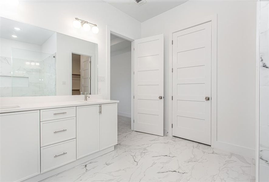 Full bathroom with double vanity, marble look tiles, a marble finish shower, and recessed lighting